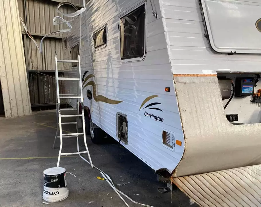 The side of a caravan that is under repairs, with a ladder positioned next to it.