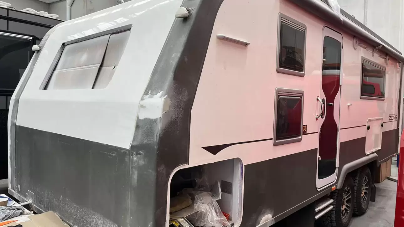 Black and white caravan that is currently undergoing repairs, parked inside a warehouse.