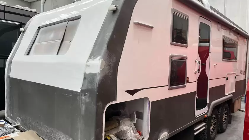 Black and white caravan that is currently undergoing repairs, parked inside a warehouse.