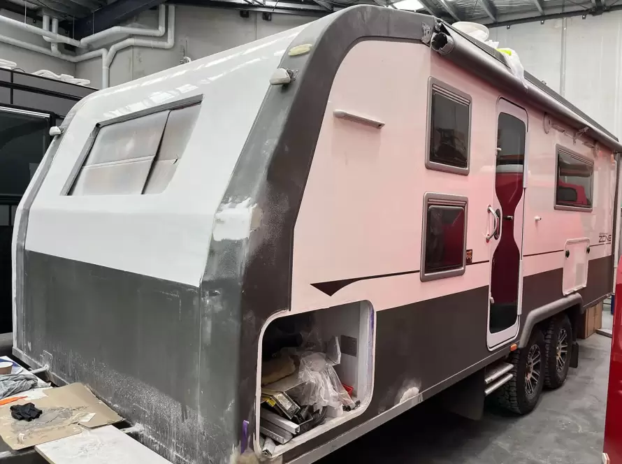 Black and white caravan that is currently undergoing repairs, parked inside a warehouse.