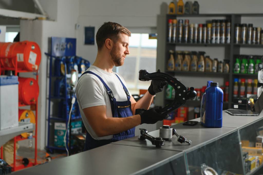 A mechanic inside a shop holding up a spare part of motor vehicle